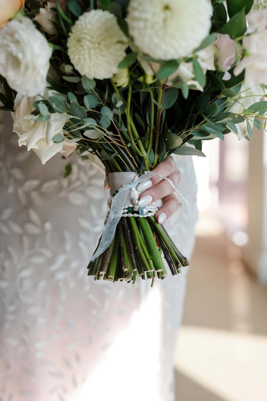 Bride holds the stem of floral bridal bouquet. 